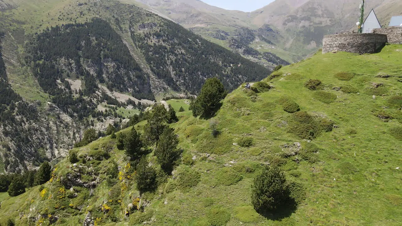 Aerial View Of A Drone Flying Backwards Showing A Couple Resting While Appreciating The Impressive Mountain Scenery Of The Pyrenees