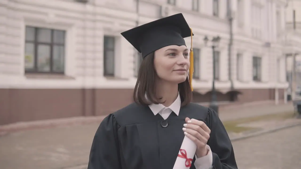 Pretty Girl Graduate Student In Gown And Cap With Diploma Looking At The Camera And Smiling