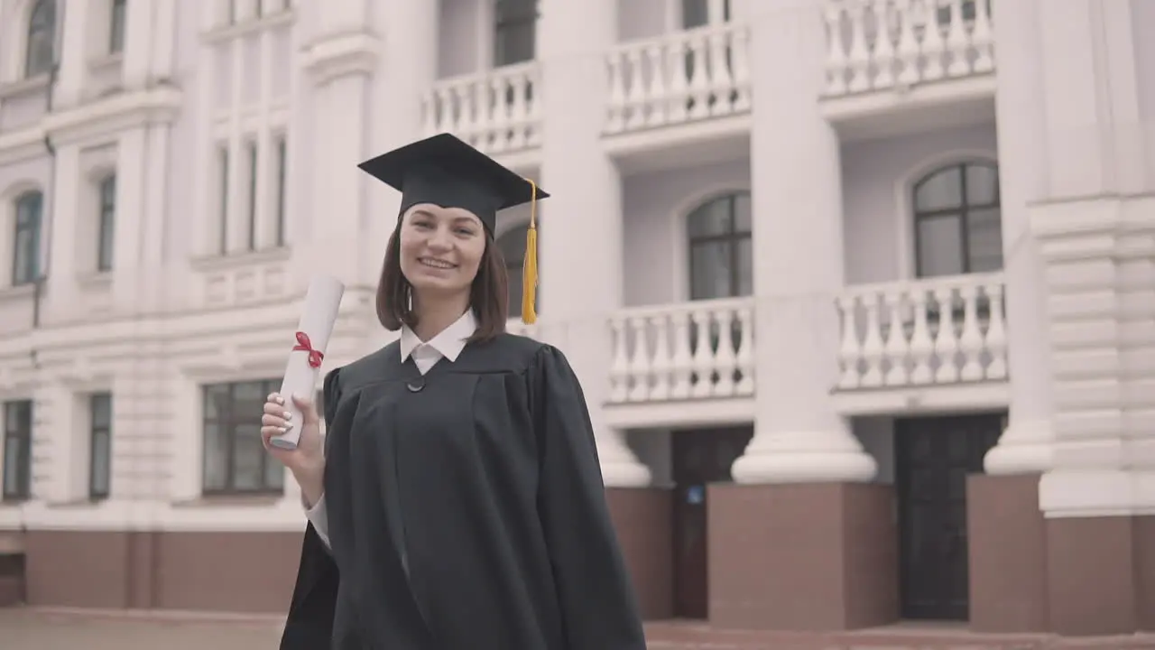 Pretty Girl Graduate Student In Gown And Cap With Diploma Looking At The Camera And Celebrating