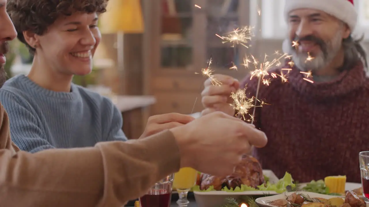 Family Sitting At Table At Christmas Meal Holding Sparklers