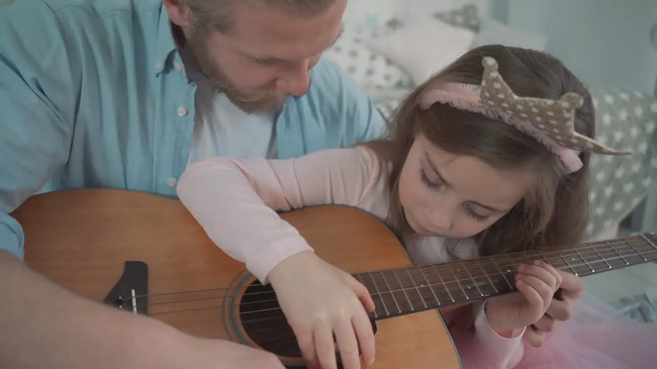 Little Daughter Dressed As A Princess Plays Guitar With Her Daddy At Home