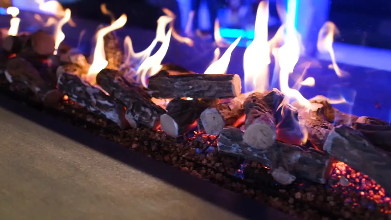 Camera truck left slowly of fire flames in a modern fireplace indoor at night with purple lighting background close up in slow motion