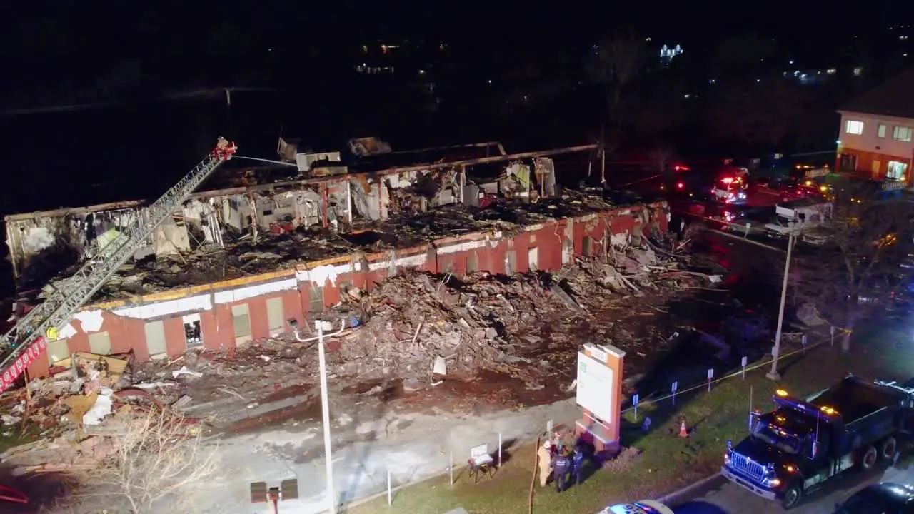 Drone shot of a motel building that was badly burned being extinguished by the local fire department using a crane at night