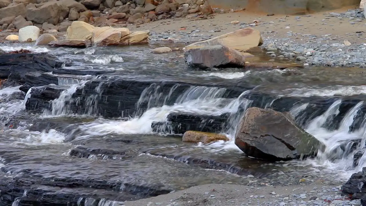 Waterfall from a wide stream flowing over rocks creating a small waterfall on beach in Kenai Peninsula of Alaska