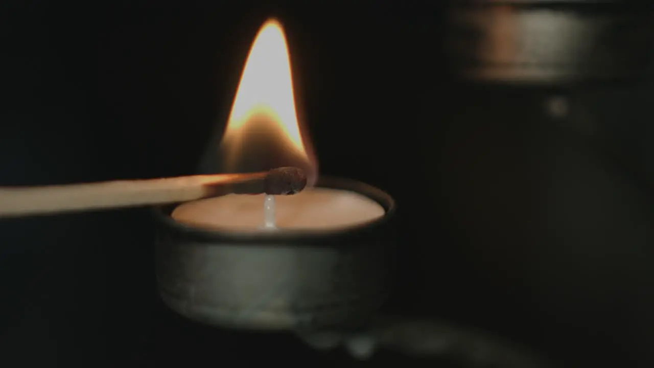 Close up of a tealight in a silver candleholder being lit by a flaring match stick with a dark background a night