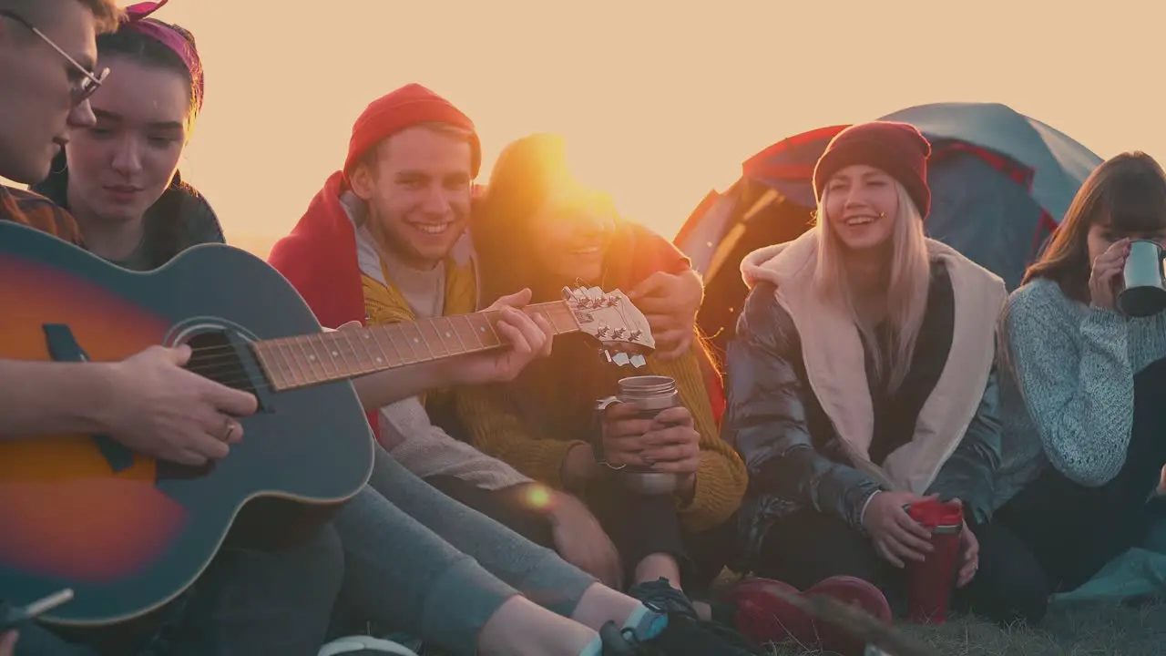 happy hikers listen to guitar sitting at bonfire in camp