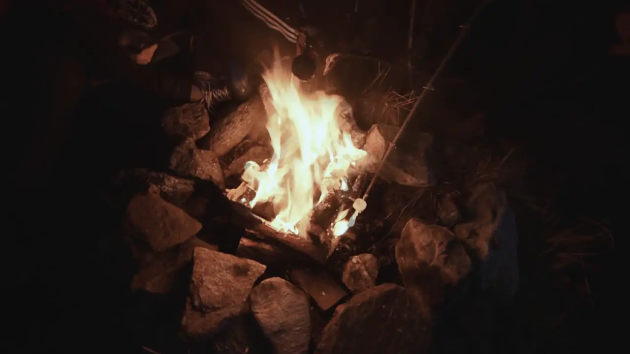 campfire bonfire with stones around in the dark with hands holding marshmallow inside the fire