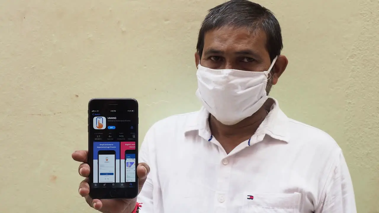 Portrait of an Indian man wearing face mask showing mobile phone with Umang app towards the camera