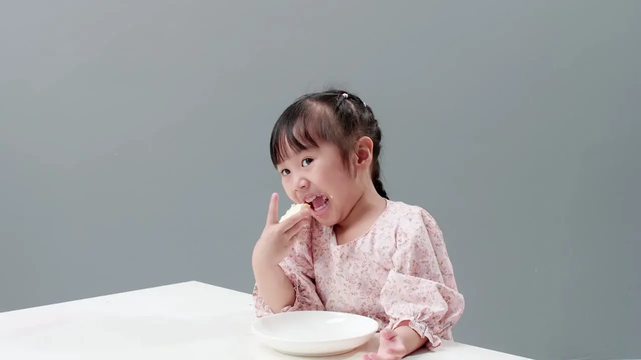 Happy little Asian girl rub her eyes smile and enjoy eaing crispy butter toast at home