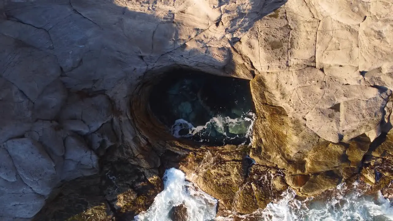 Top down aerial of natural circular shaped pool sea waves crashing against