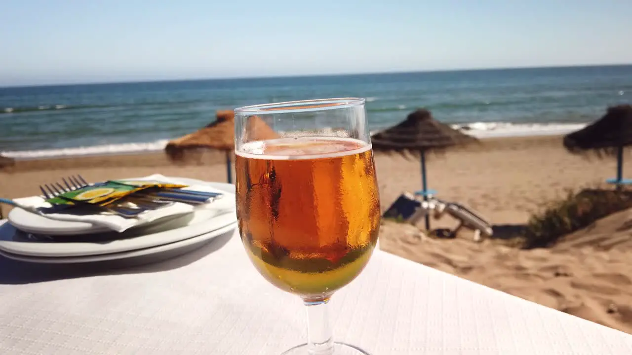 cold refreshing beer glass on a table with sea view and a Spanish beach in Marbella filmed in 4k