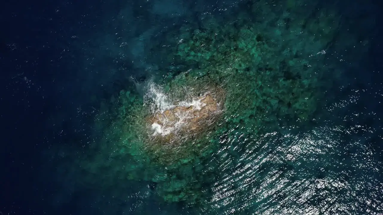 Drone with a top down view of a rock pinnacle just breaking the service surrounded by a coral reef