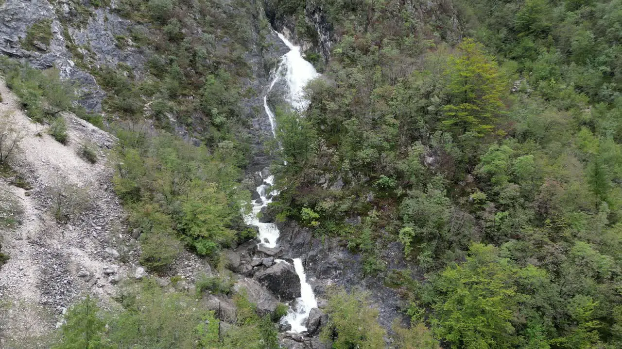 Waterfall cascading though trees Lake Bohinj Slovenia rising crane drone aerial view