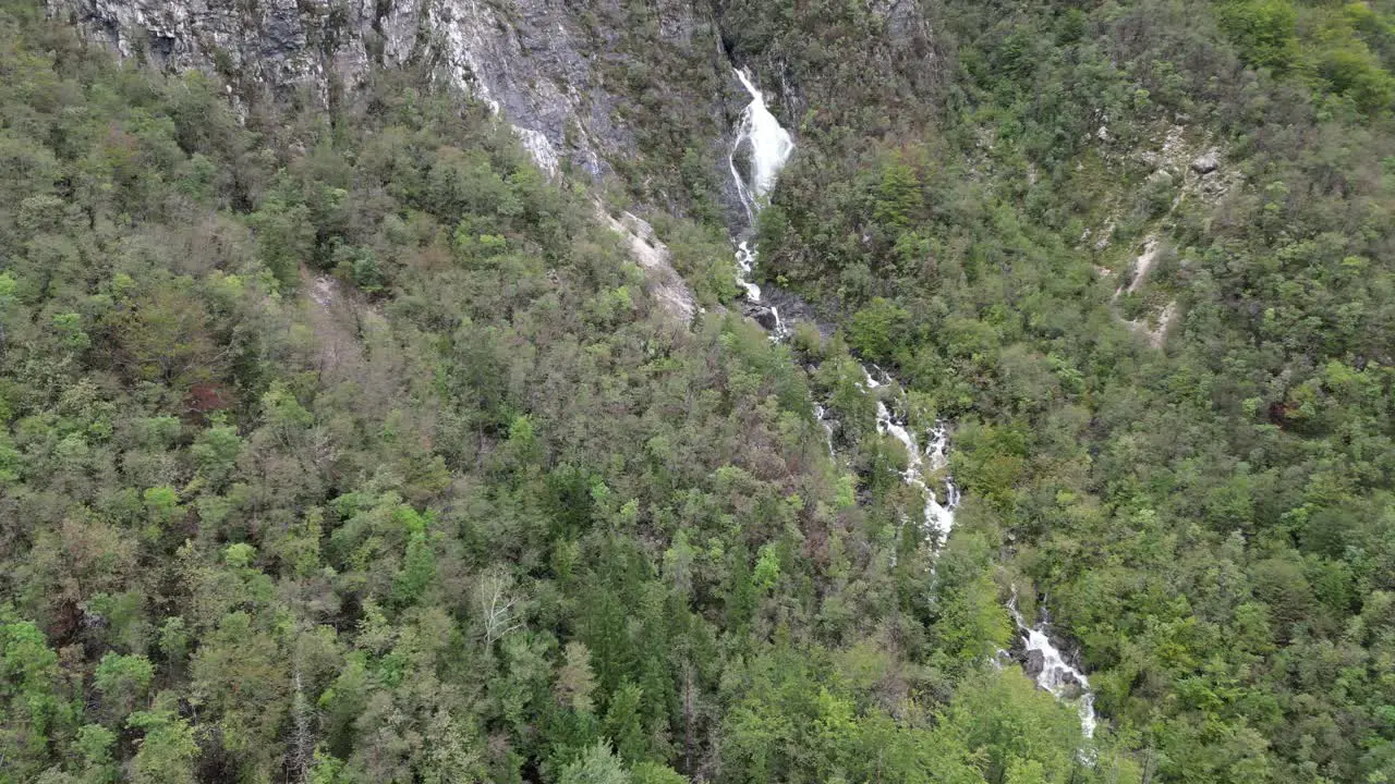 Waterfall cascading through trees Lake Bohinj Slovenia pull back reveal drone aerial view