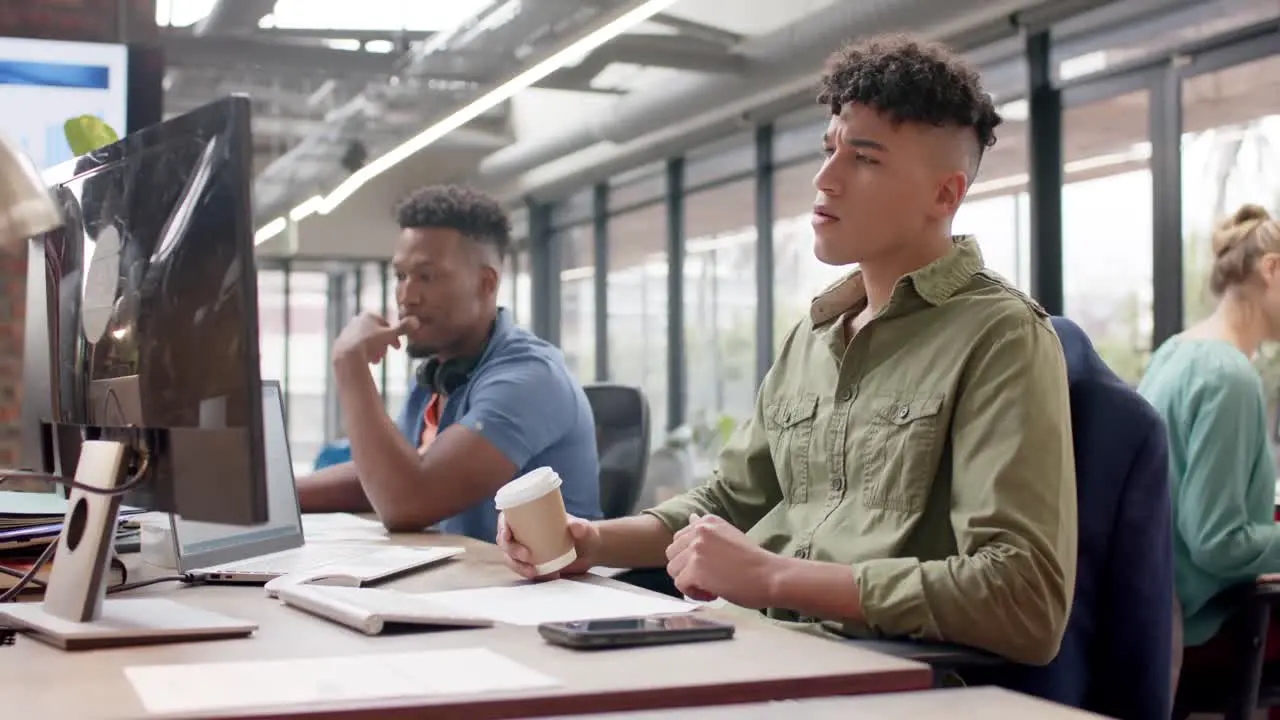 Two diverse male casual business colleagues working at computers and drinking coffee slow motion