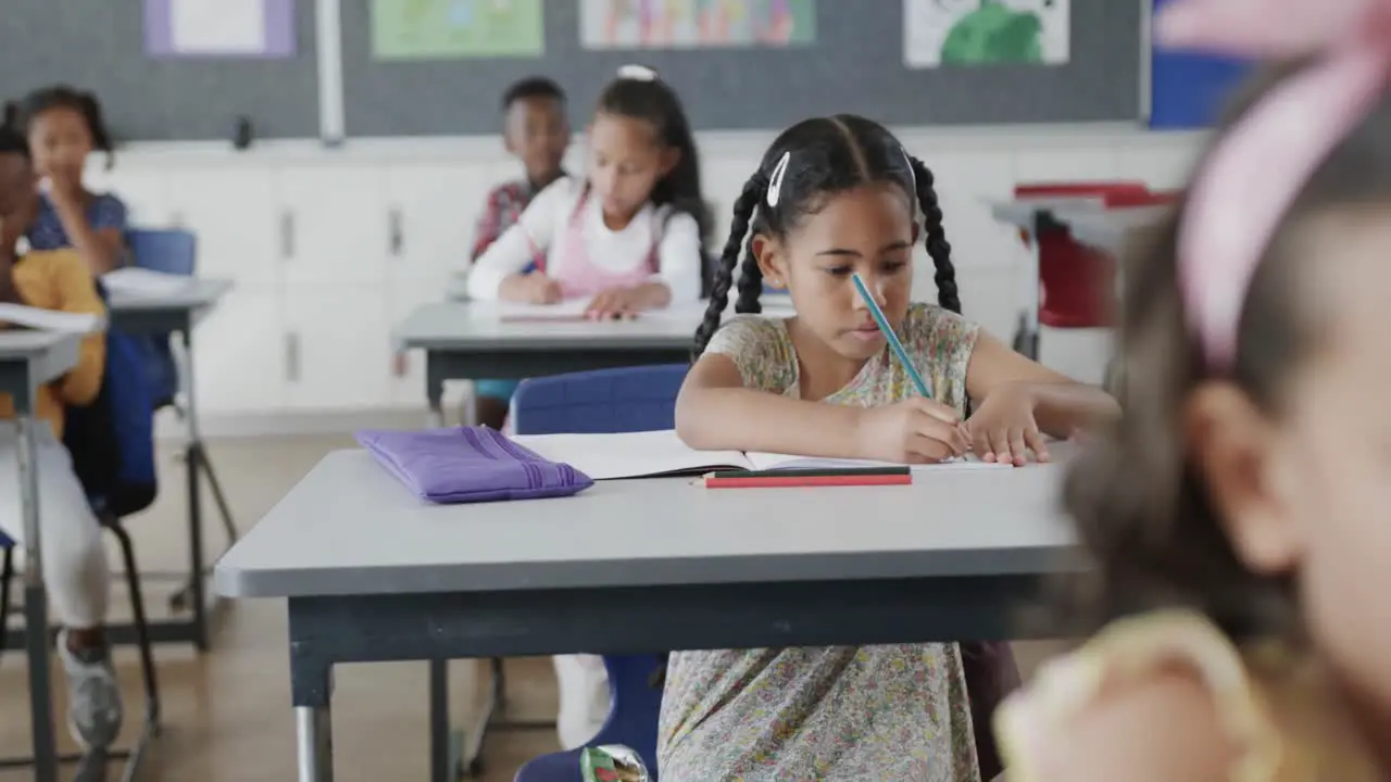 Focused diverse schoolchildren writing at desks in elementary school classroom slow motion