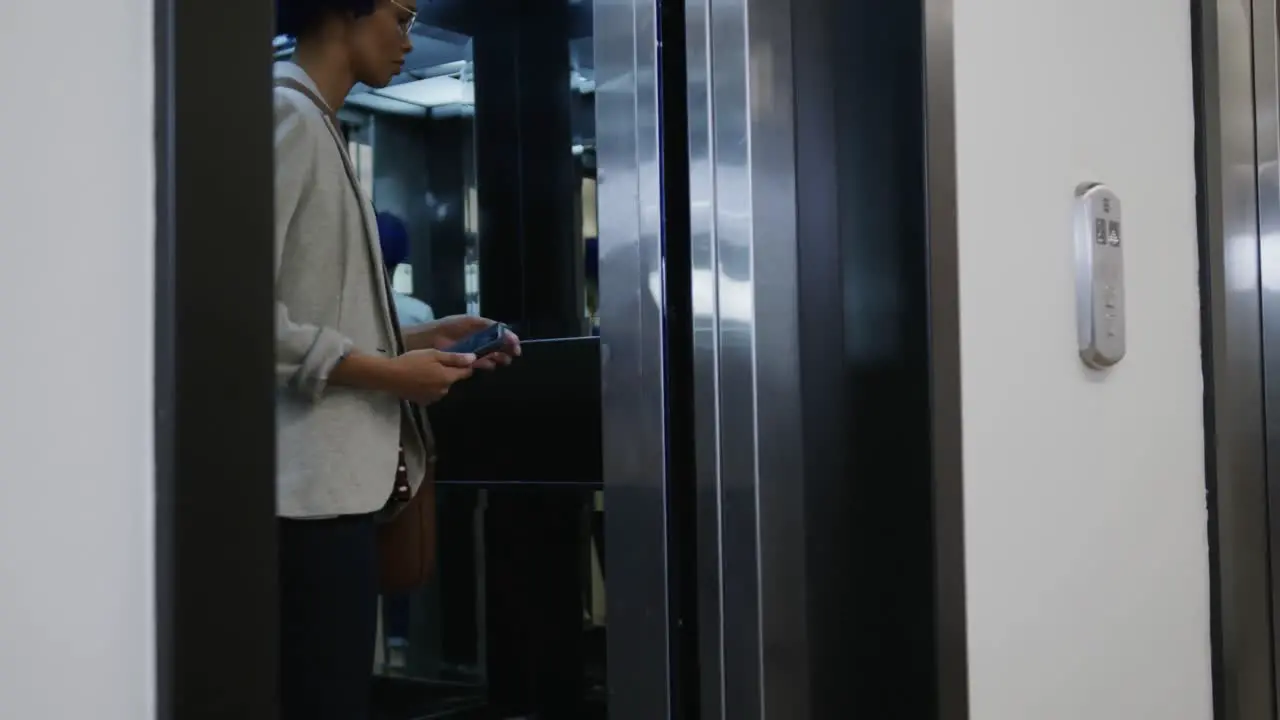 Biracial businesswoman with blue afro using smartphone and entering elevator in office slow motion