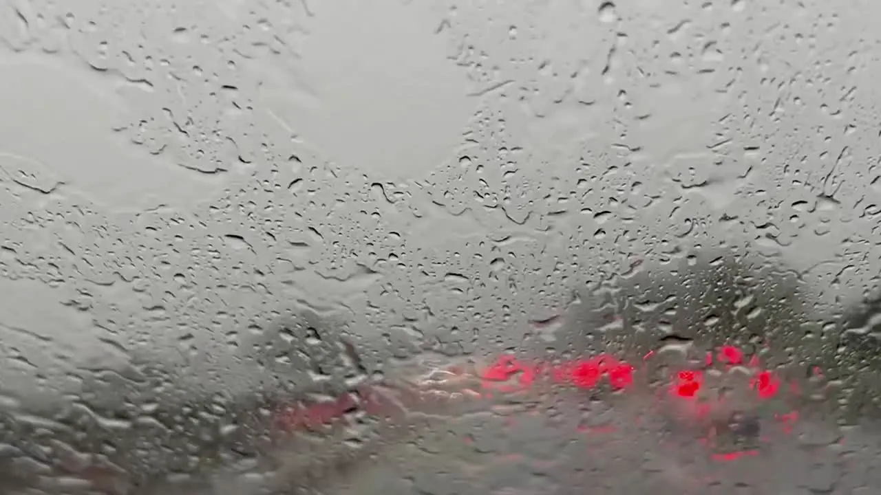 Pouring rain over windscreen and red blurred lights of car traffic in background with wiper cleaning windshield from raindrops