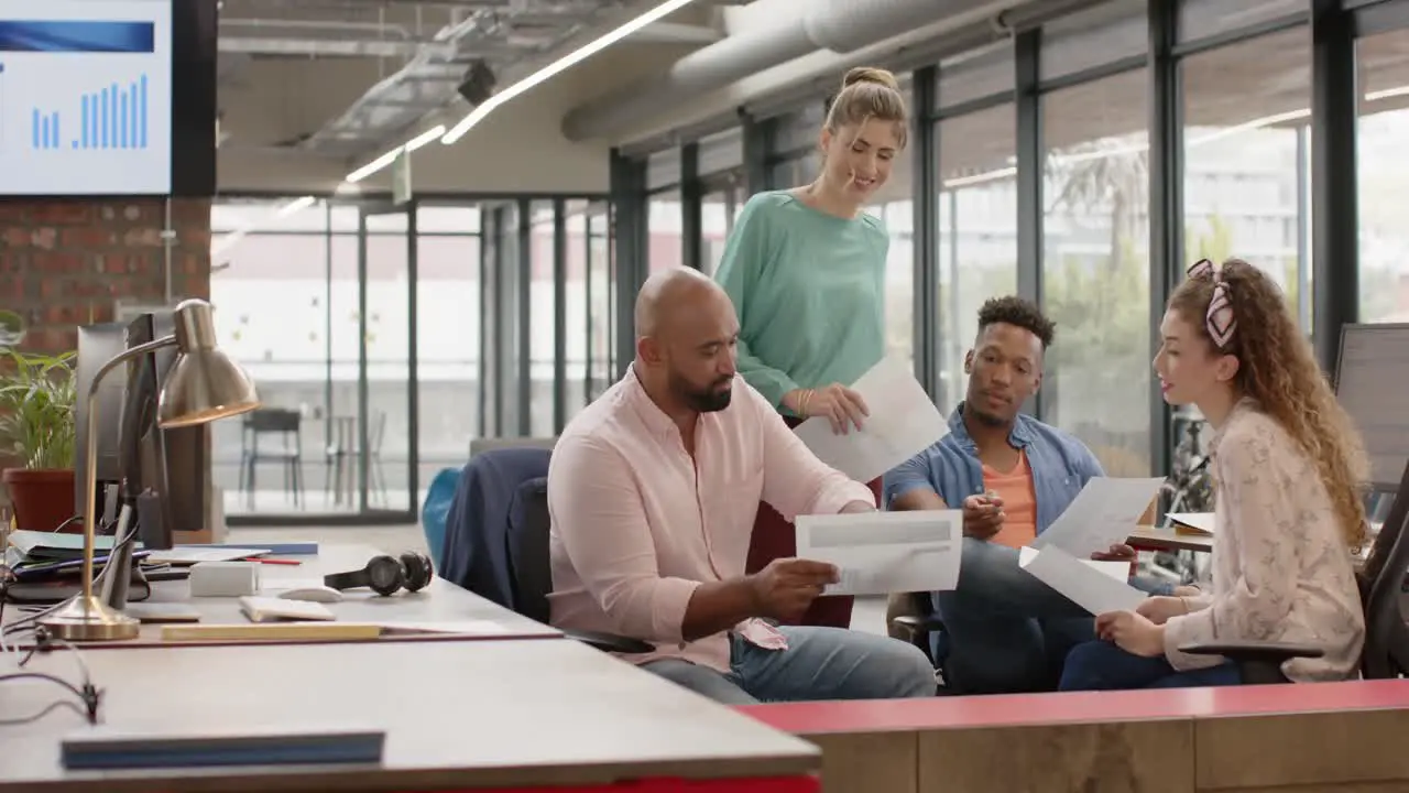 Happy diverse creative business colleagues in discussion at desk in casual office in slow motion