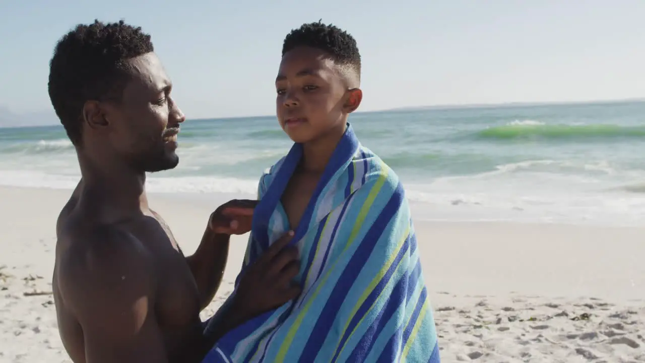 Smiling african american father toweling off his son on sunny beach