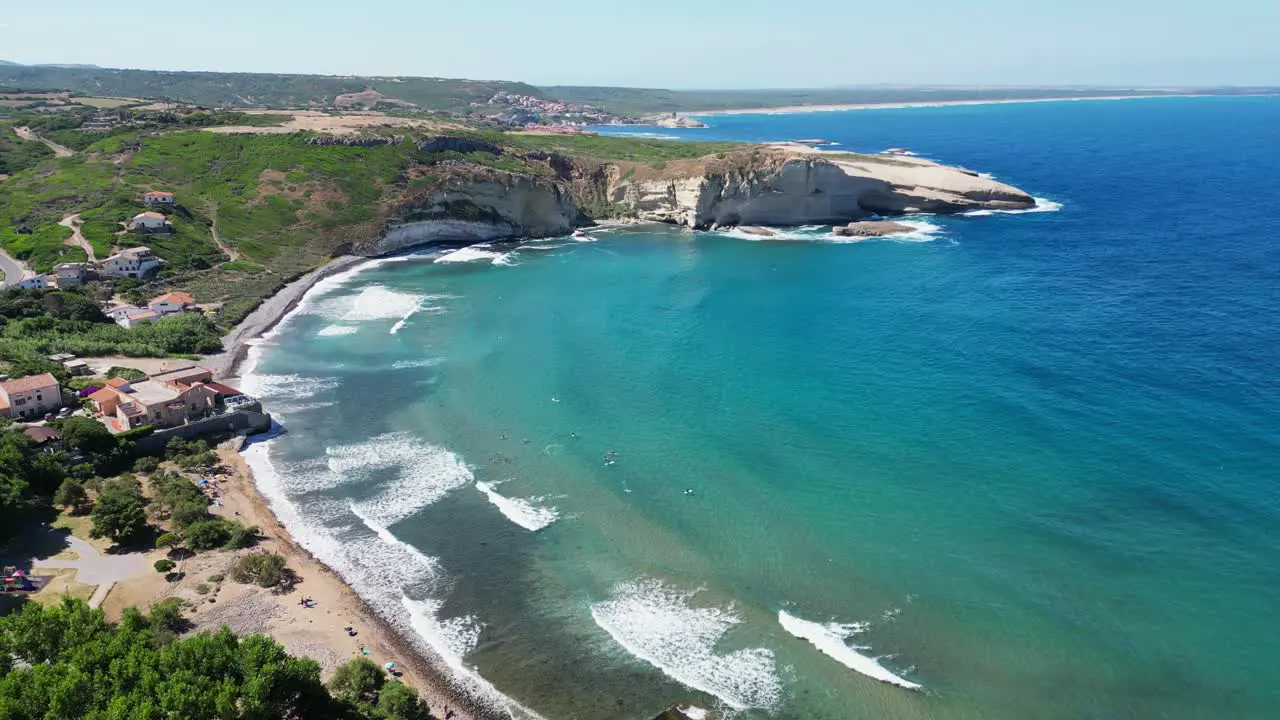 Surfers in blue bay at S' Archittu beach town west coast of Sardinia 4k Aerial