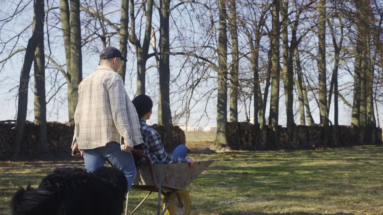 Caucasian man carrying his partner on a wheelbarrow in the countryside Their dog walks around them