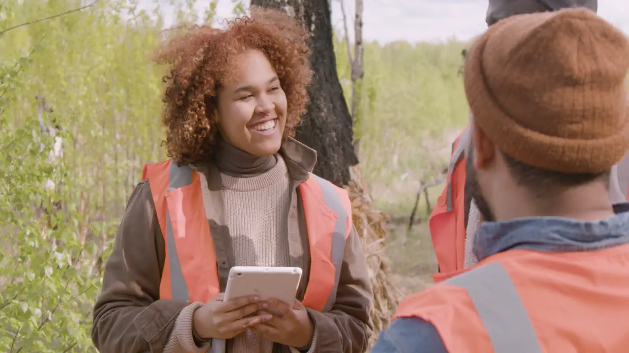 Close-up view of an african american woman activist holding a tablet and talking with her coworkers in the forest while they deciding where to plant trees