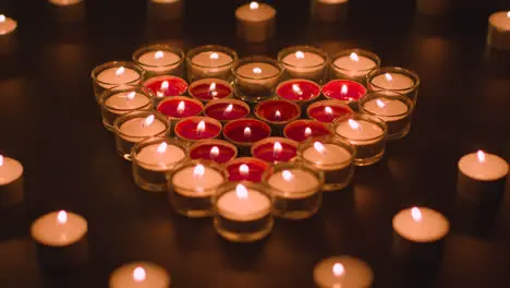 Pull Focus Shot Of Romantic Red And White Candles In the Shape Of A Heart On Black Background