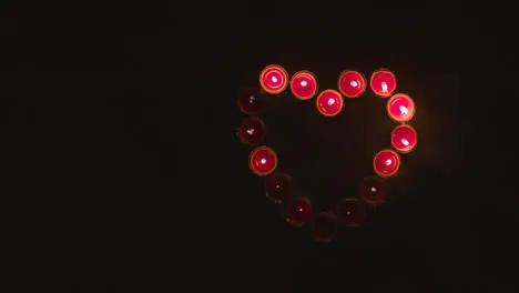 Overhead Shot Of Lit Red Candles In Shape Of Romantic Heart Being Blown Out On Black Background