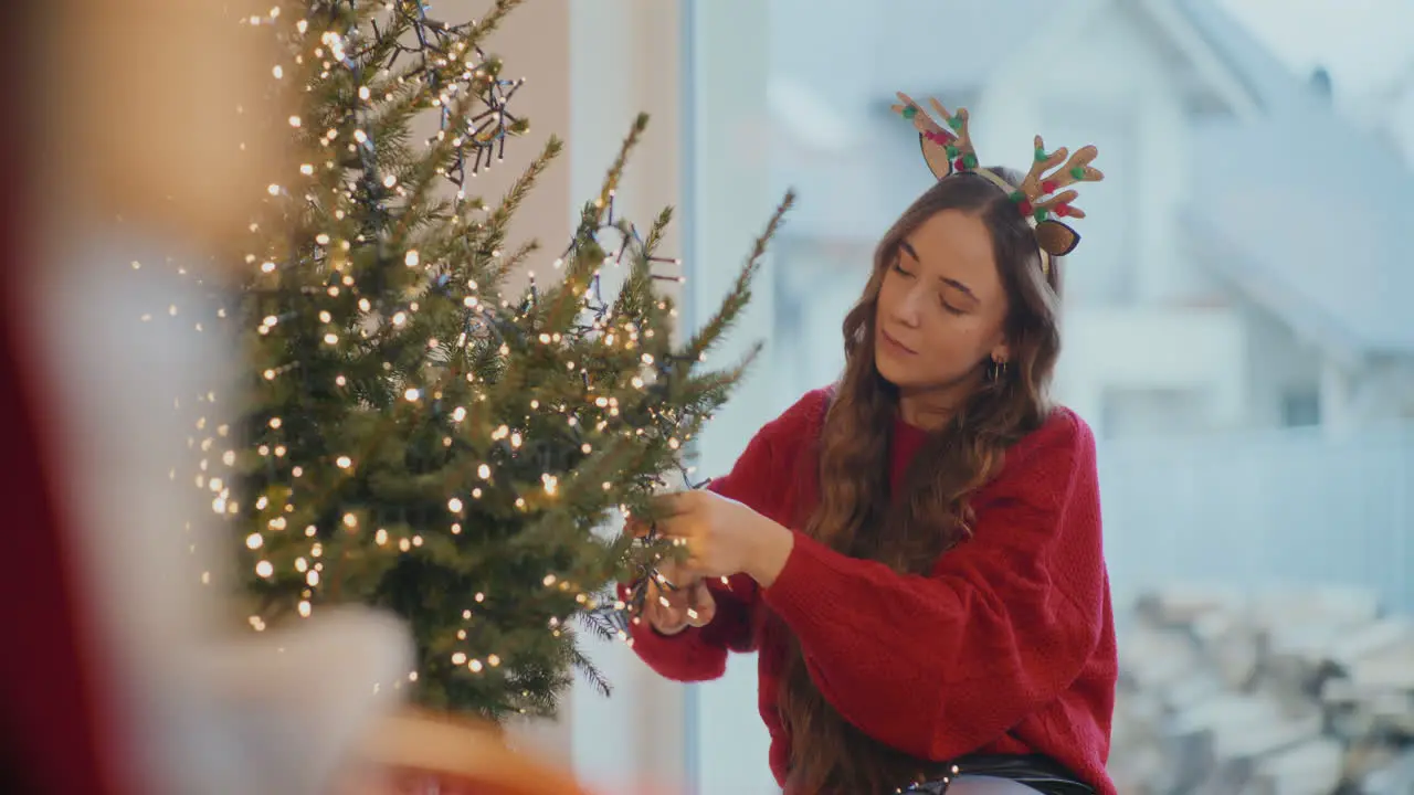 Woman decorating tree with glowing lights at home