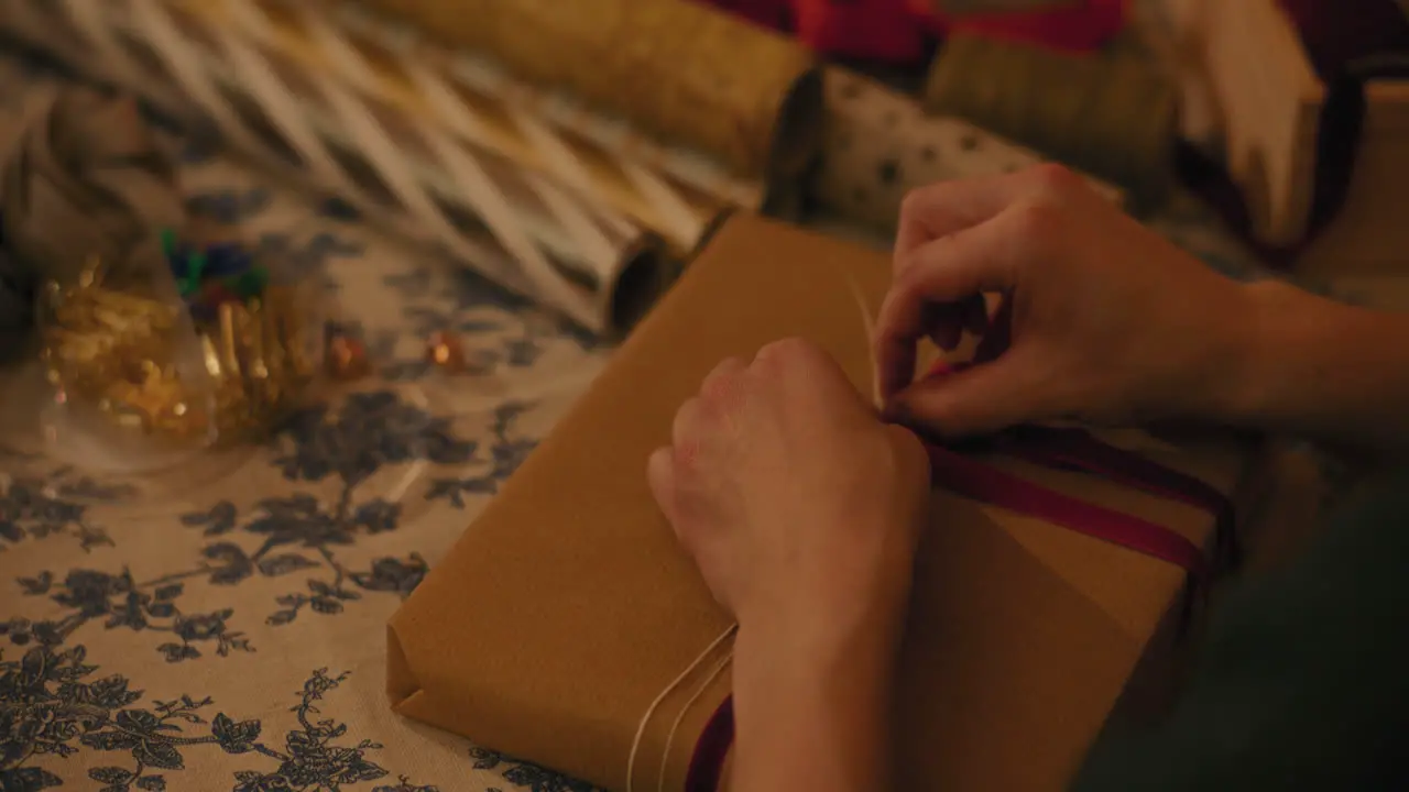 Woman tying ribbon on gift box at table