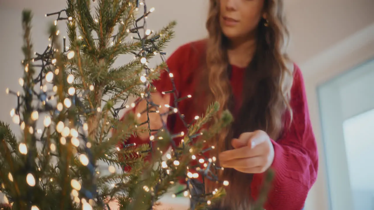 Woman decorating Christmas tree with glowing lights