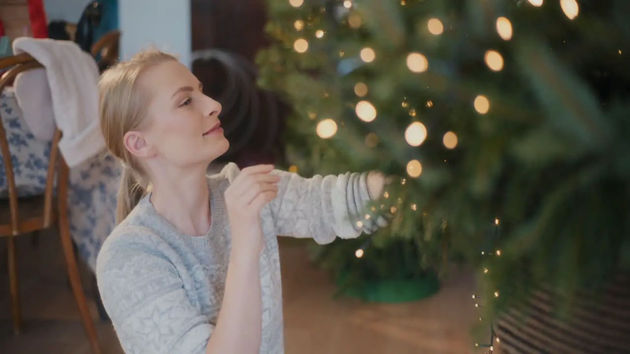 Woman with illuminated lights decorating Xmas tree