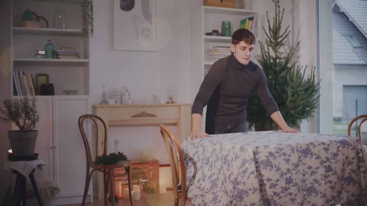 Young man setting tablecloth on table