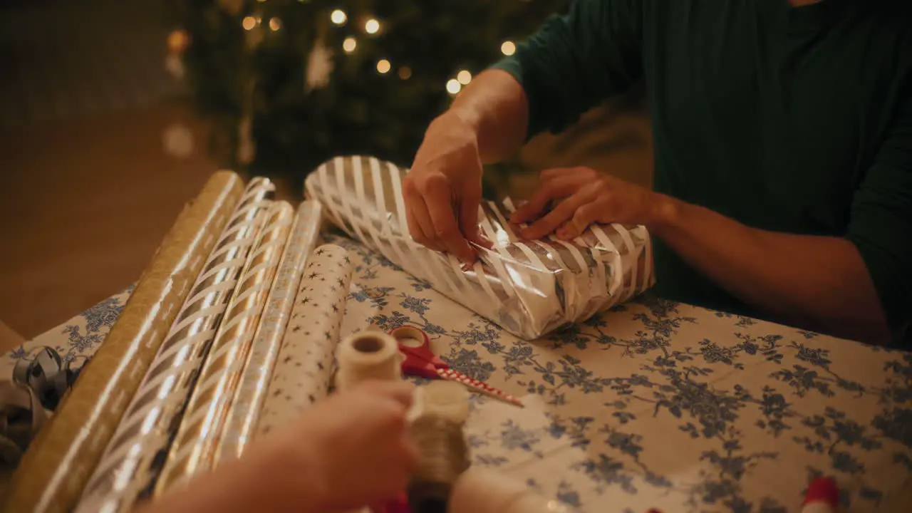 Man wrapping gift paper on box at table