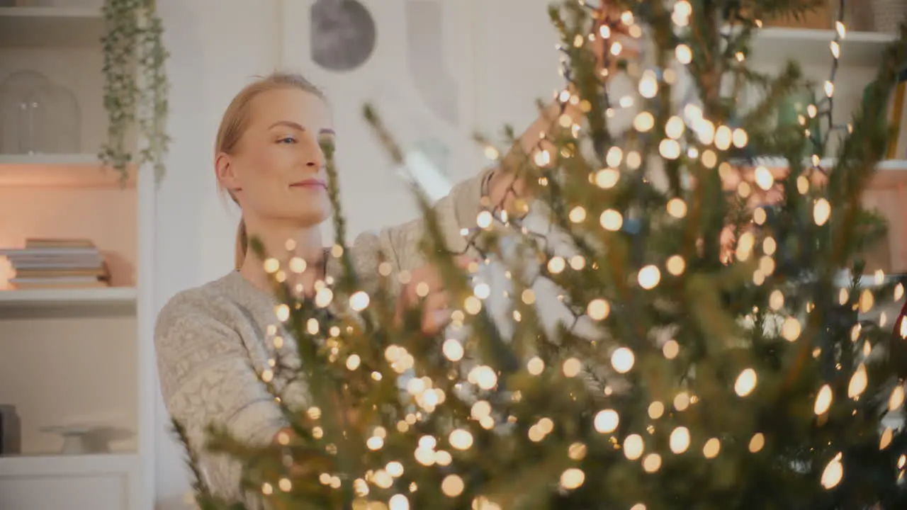 Woman decorating Christmas tree with glowing led lights