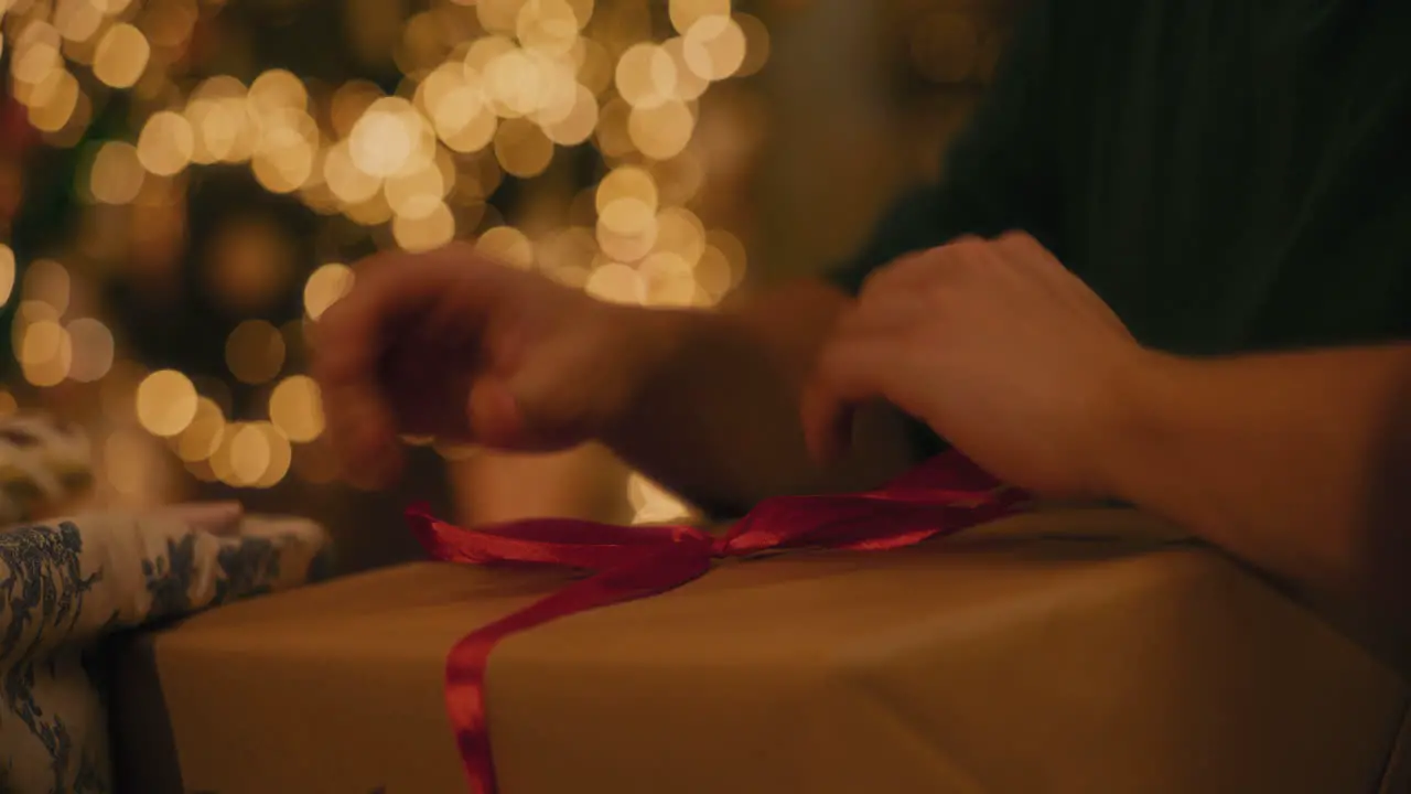 Man tying ribbon to Christmas gift box at home