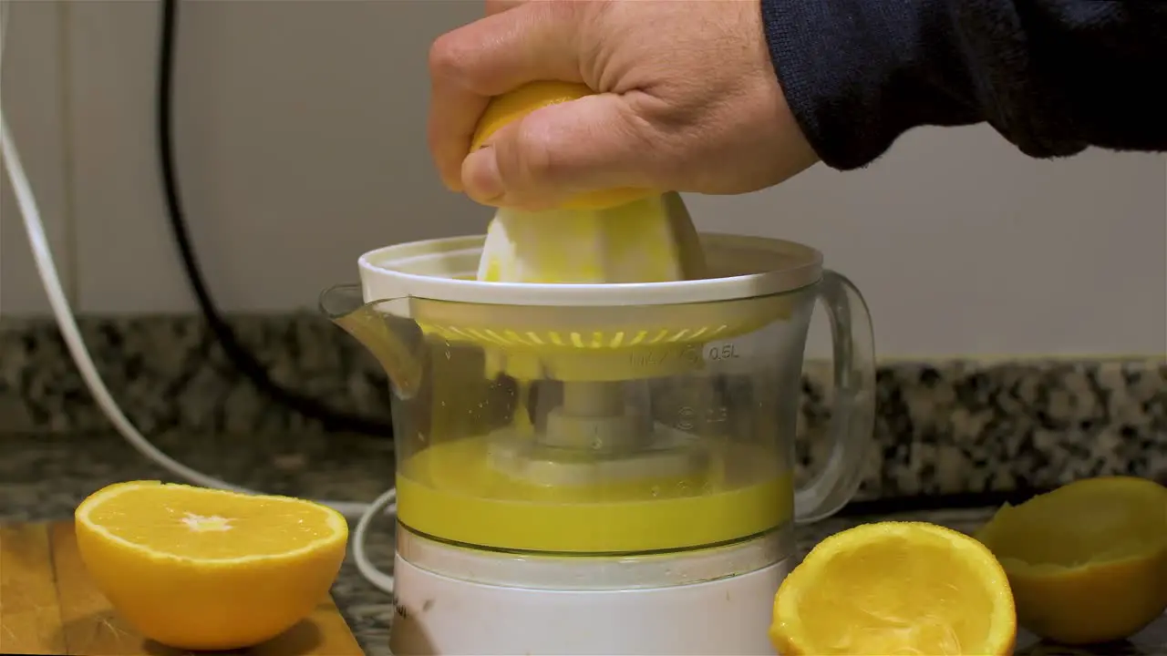 View of a hand squeezing half an orange in a orange juicer in the kitchen