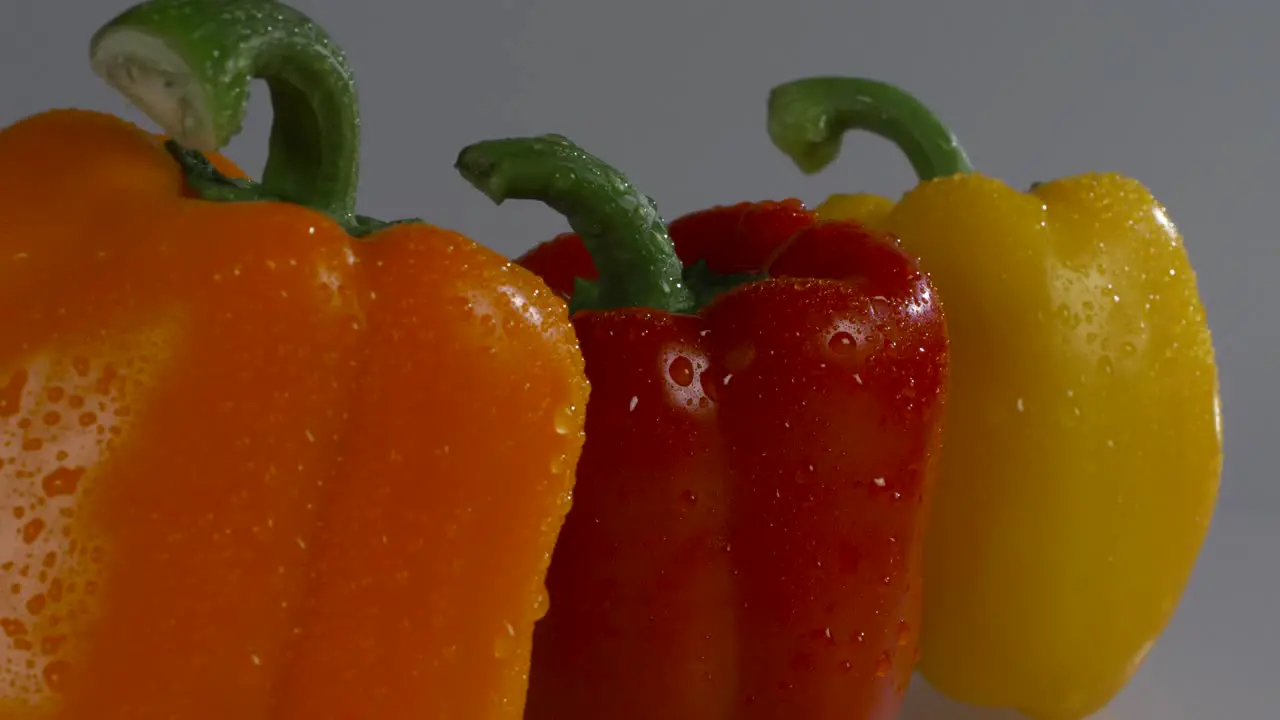 Fresh red yellow and orange peppers on a white background with water droplets