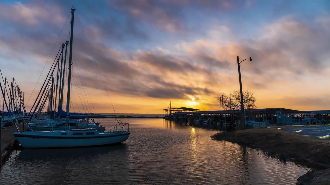 Boats moored at dock rock as clouds pass over golden sunrise reflecting on water