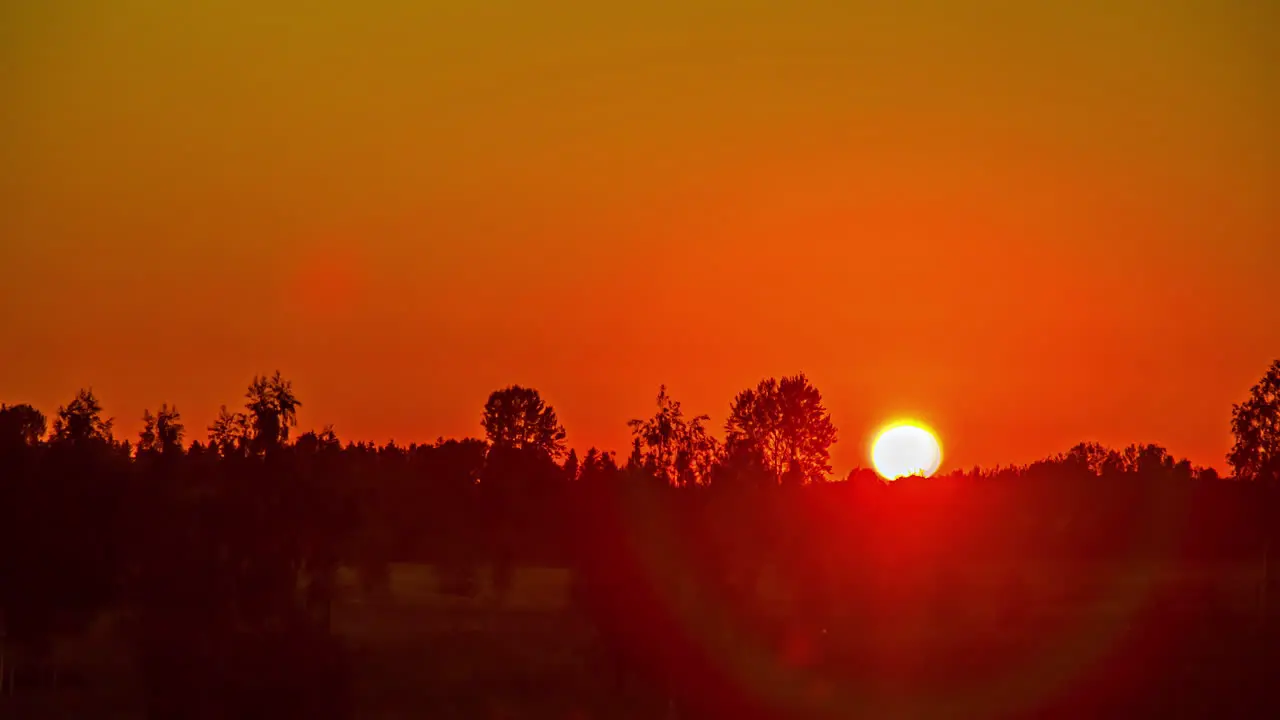 A bright fiery sunset over the countryside turns to orange at dusk time lapse