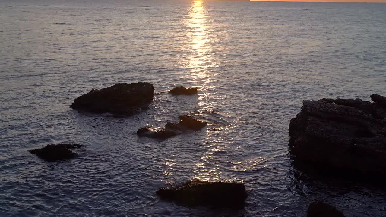 Slow cinematic tilt up over rocks in ocean during sunrise