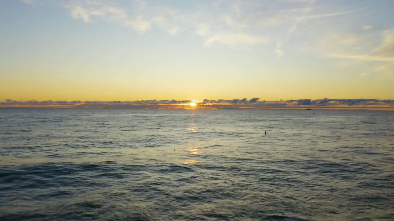 Low Aerial Shot as the sun peaks through distant clouds during the early morning sunrise over Lake Michigan