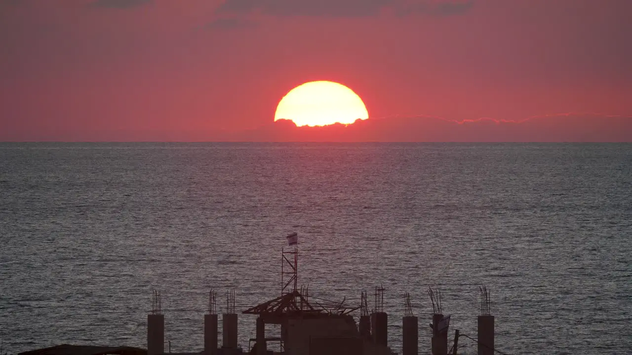 Red sun setting in the sea in Gaza with Israel flag in front dramatic sunset footage