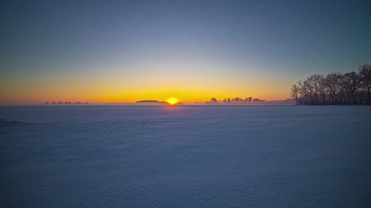 Bright golden sunrise on a hazy winter day with no clouds across a field of snow time lapse