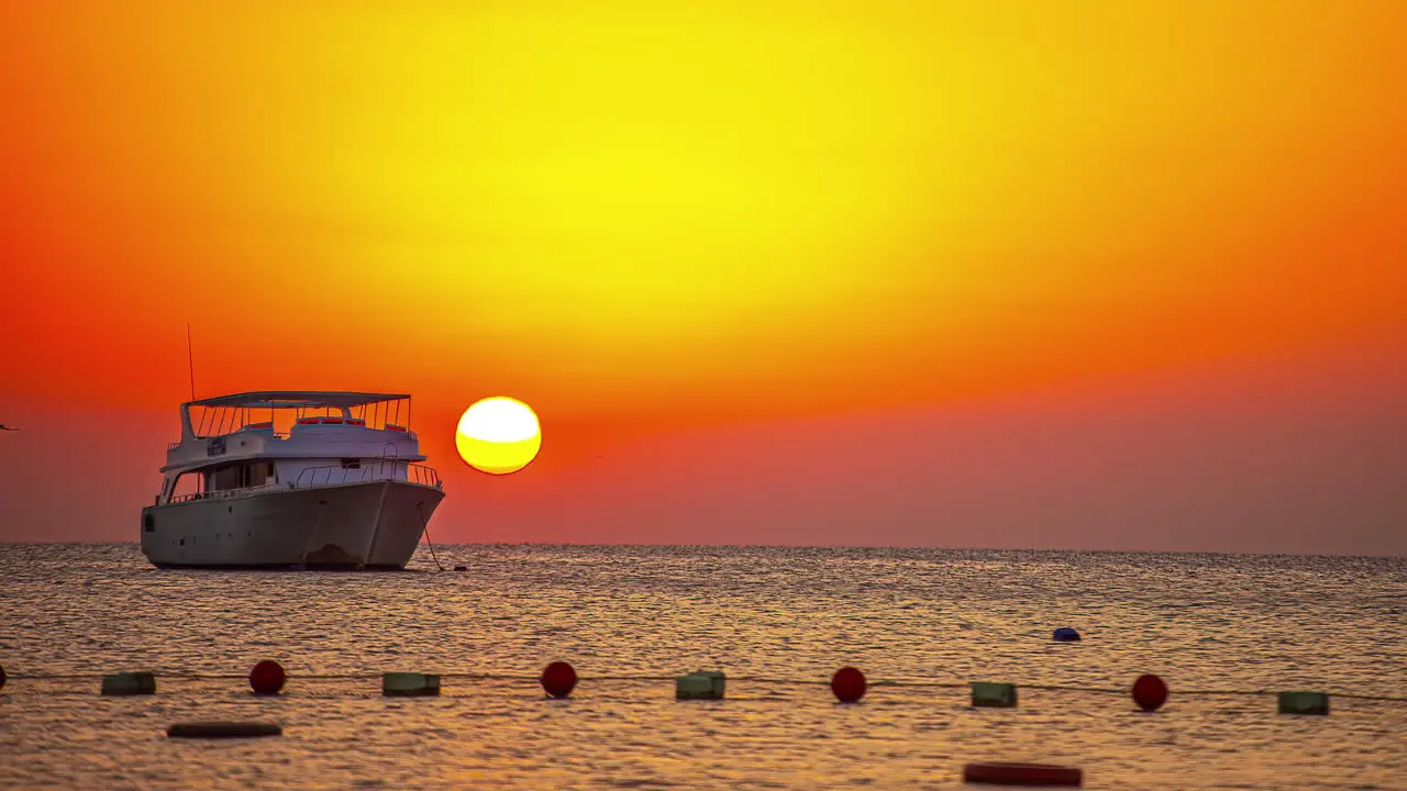 Luxury Boat anchored on Ocean water in front of orange sunset time in background time lapse