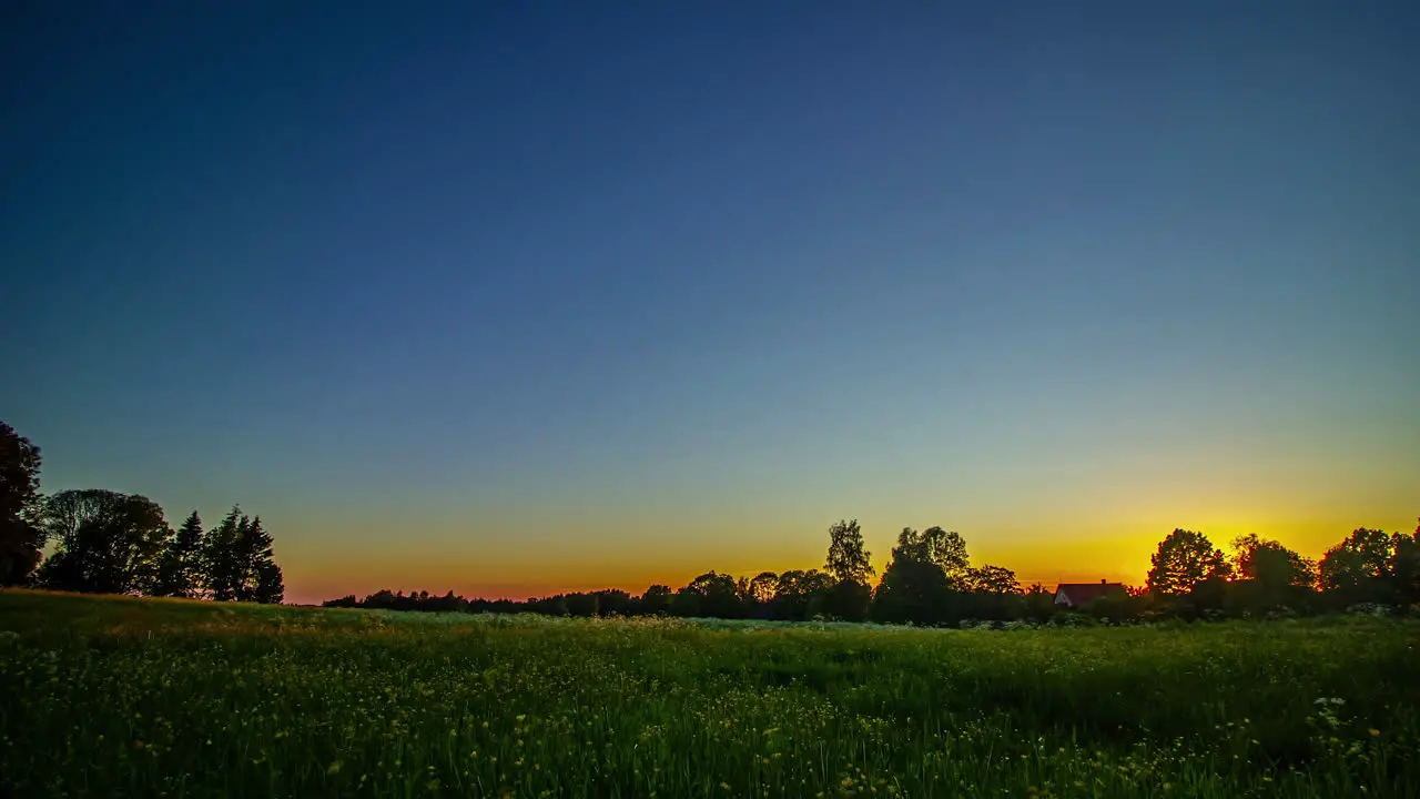 Timelapse shot of beautiful sunset over green grasslands with the view of cottage in background at dusk