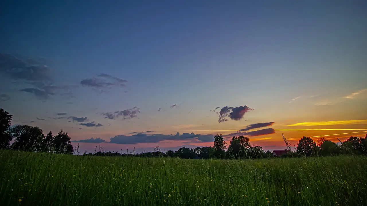 Timelapse shot of beautiful sunset green grasslands in front of a cottage at dusk