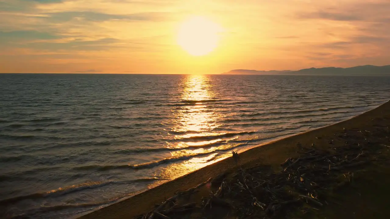 Cinematic backwards aerial drone footage of the sunset at a sandy beach at the seaside near Alberese in the iconic Maremma nature park in Tuscany Italy with waves islands and a dramatic red sky