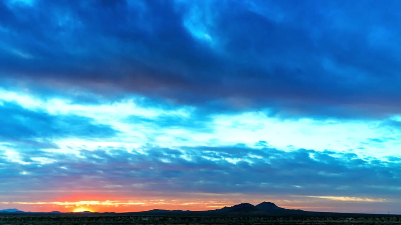 The sun sets with brilliant colors in the cloudscape in this desert time lapse wide angle static